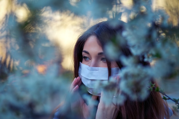 Bouchent le portrait de jeune fille sous un arbre en fleurs avec un masque du coronavirus.