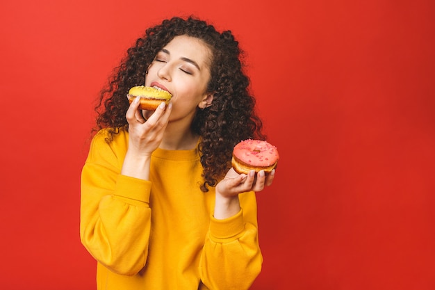 Bouchent le portrait d'une jolie jeune fille satisfaite de manger des beignets isolés sur fond rouge.