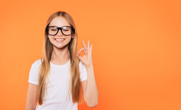 Bouchent le portrait d'une petite fille blonde heureuse, drôle et belle dans des verres pose sur fond jaune. Étude, éducation, école, université, collège, concept d'études supérieures