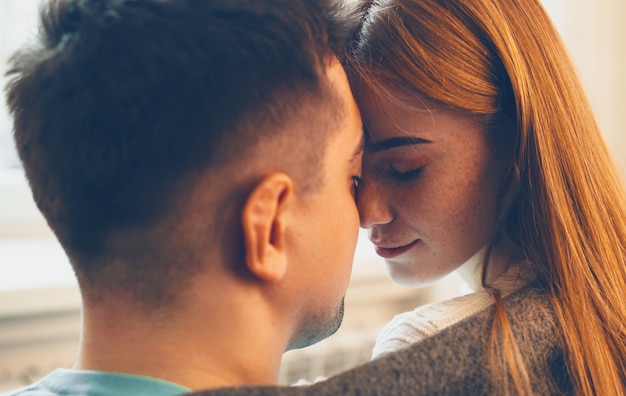 Photo bouchent le portrait de vue latérale d'une belle femme aux cheveux rouges et taches de rousseur et son homme assis face à face avec les yeux fermés avant de s'embrasser à la maison.