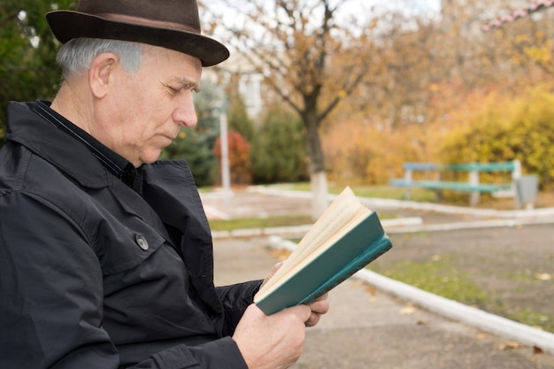 Bouchent le portrait de vue latérale d'un homme âgé dans un pardessus et un chapeau lisant son livre à l'extérieur