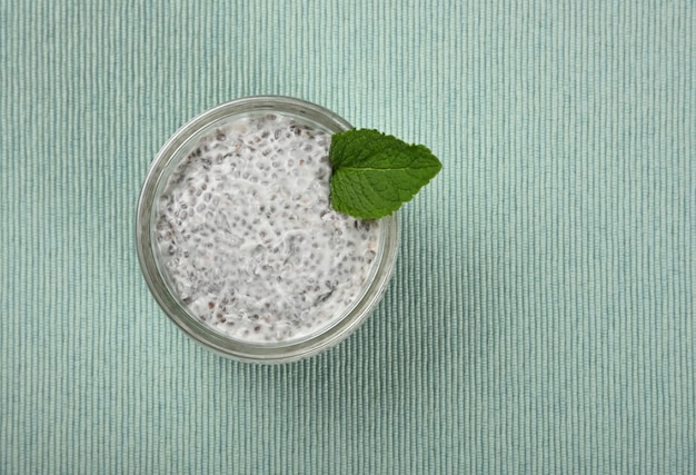 Bouchent un pot en verre transparent de pudding de graines de chia dessert avec du lait de coco sur nappe menthe sarcelle, vue de dessus élevée, directement au-dessus