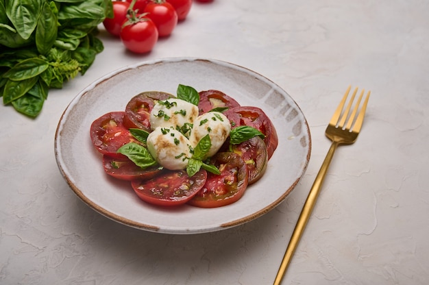 Bouchent la salade caprese avec des tomates rouges, du basilic et de la mozzarella dans une assiette blanche et une fourchette dorée