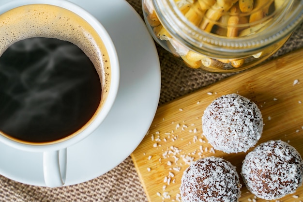 Photo bouchent la tasse de café noir et de délicieux bonbons à la noix de coco sur une planche de bois.