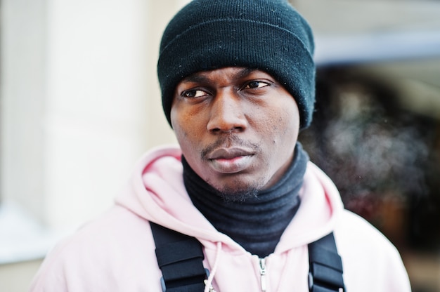 Bouchent la tête de l'élégant homme afro-américain de style urbain en rose à capuche et chapeau noir posé. Respiration gelée.