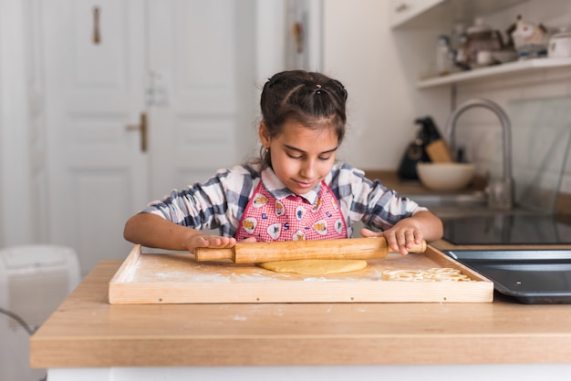 Photo bouchent la vue sur la belle petite fille à rouler la pâte dans la cuisine. fille mains rouler la pâte sur la table de cuisine. les mains de l'enfant cuisiner avec un rouleau à pâtisserie.