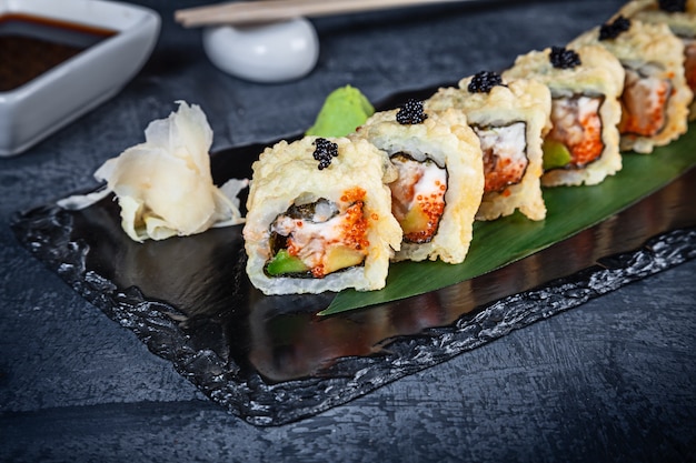 Bouchent la vue sur l'ensemble de rouleaux de sushi. Rouleau chaud à l'anguille et au caviar servi sur pierre noire sur fond sombre. Cuisine japonaise. Copiez l'espace. Sushi servi pour le menu. Nourriture saine, fruits de mer