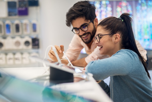 Bouchent la vue latérale du charmant couple heureux jeune étudiant heureux excité souriant à une nouvelle tablette dans un magasin de technologie.