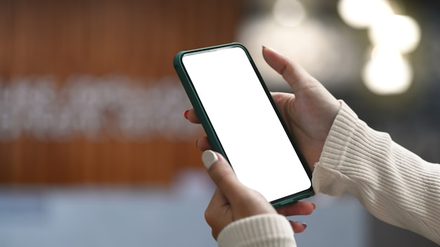 Bouchent la vue des mains de femme tenant une maquette de téléphone intelligent avec arrière-plan flou de bureau.