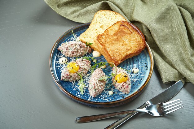 Bouchent la vue sur le tartare de boeuf frais avec du pain, des œufs et dans une assiette. Veau tartare maison sur table en bois