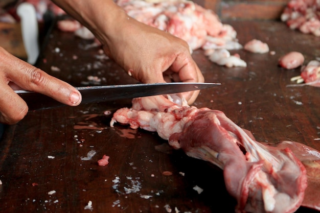 Boucher coupant la viande crue de jambe de chèvre sur une planche à découper en bois avec le couteau