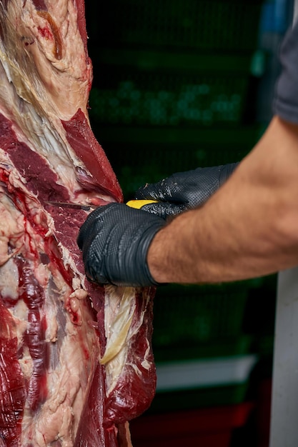 Un boucher coupe de la viande de vache dans un entrepôt avec un couteau.