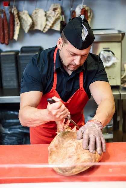 Boucher désosser un jambon dans une boucherie moderne