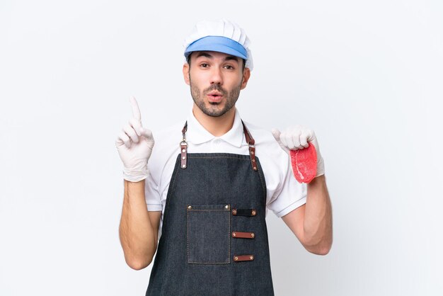 Boucher homme caucasien portant un tablier et servant de la viande fraîchement coupée sur fond blanc isolé dans l'intention de réaliser la solution tout en levant un doigt vers le haut