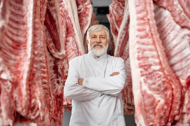 Boucher posant, debout entre des rangées de carcasses de porc.