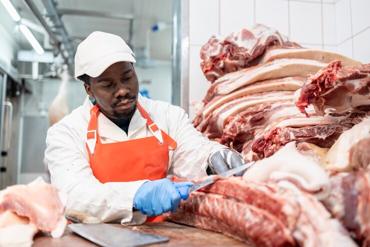 Boucher professionnel avec un couteau tranchant travaillant avec de la viande crue à l'abattoir