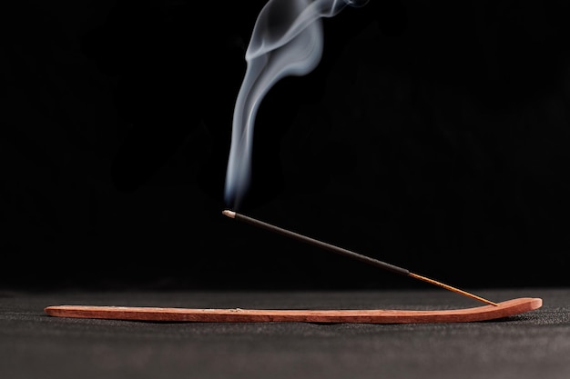 Photo boucles de fumée de bâton d'encens brûlant dans un support en bois pour la relaxation et la méditation fond noir