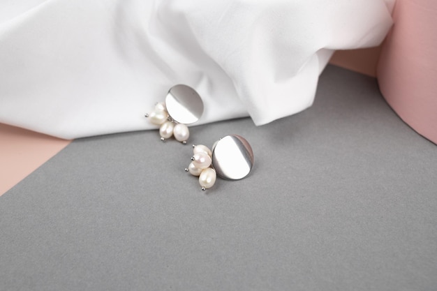 Boucles d'oreilles en argent à la mode sur fond de tissu blanc froissé Bijoux à la mode pour femmes avec perles Photo de haute qualité