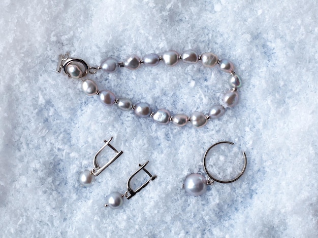 Boucles d'oreilles, bague et bracelet en perles baroques noires élégantes de luxe sur fond de neige blanche. Photo en gros plan