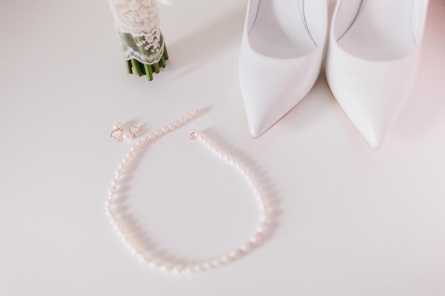 Boucles d'oreilles et collier de perles de mariage se bouchent avec des chaussures de mariage et fond de bouquet