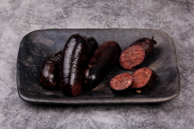 boudin entier frit et tranché sur une plaque d'argile noire, fond de pierre grise