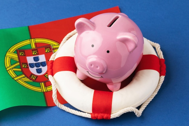 Bouée de sauvetage tirelire et drapeau sur fond bleu le concept de sauver l'économie portugaise