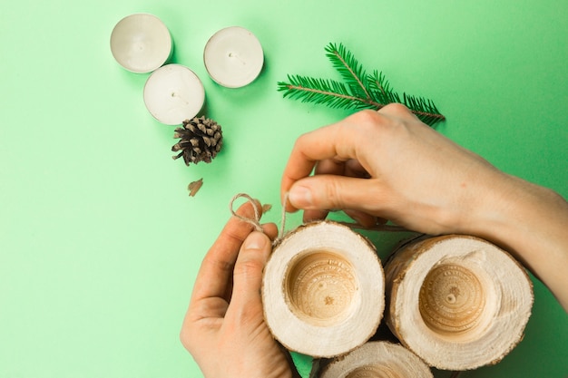 Bougeoir de Noël bricolage fait de bûches de pin, de bougies, de corde artisanale, de branches de sapin et de cônes. Les mains attachent et attachent la corde. Instructions étape par étape à plat, étape 3.