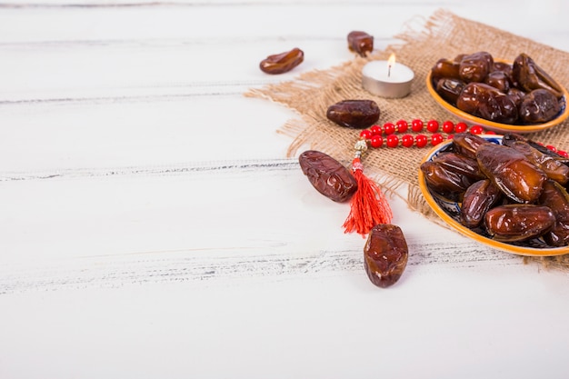 Photo bougie allumée avec assiette de dattes juteuses et perles de prière rouges sur un bureau en bois