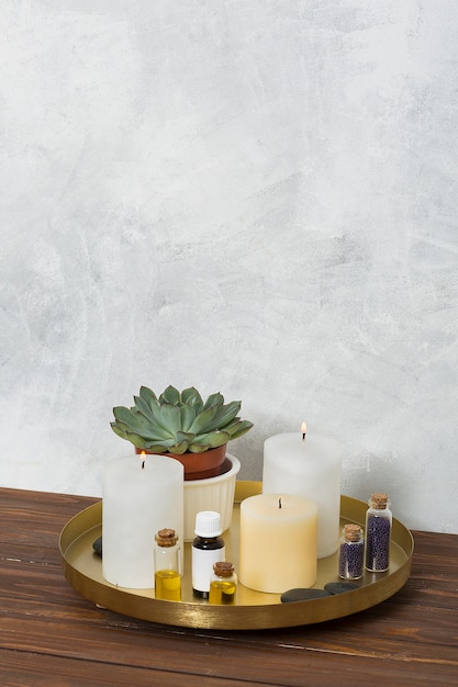 Bougie allumée; plante de cactus; graine de moutarde; la pierre et l&#39;huile essentielle sur une plaque de cuivre posée sur le bureau en bois