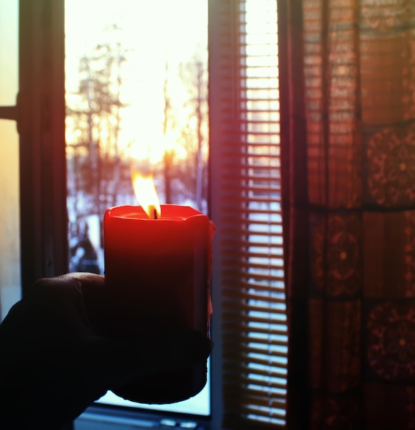 Bougie allumée rouge dans une main sur fond de lever de soleil d'hiver