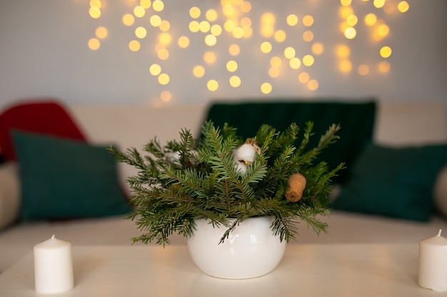 Une bougie blanche décorée de branches de sapin et de boules de verre rouge debout sur une table en bois avec une serviette en lin.