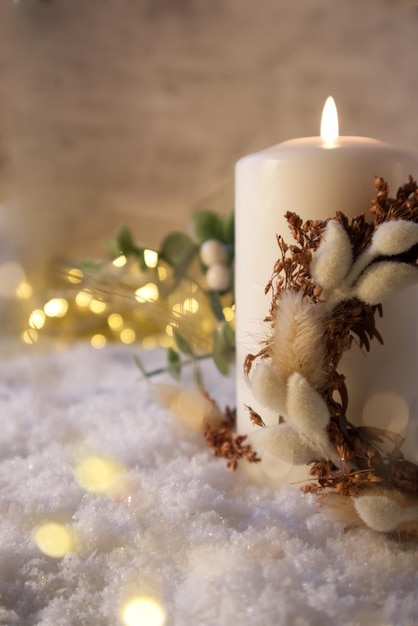 Une bougie blanche décorée d'un décor de Noël sur la neige sur fond de lumières