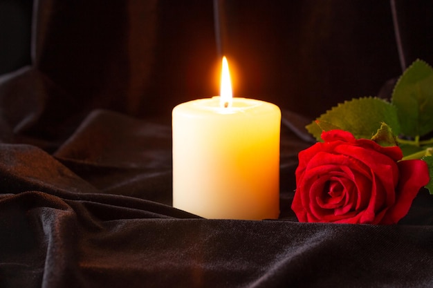 Une bougie brûlante et une rose rouge sur un fond de tissu noir le concept de condoléances et de religion