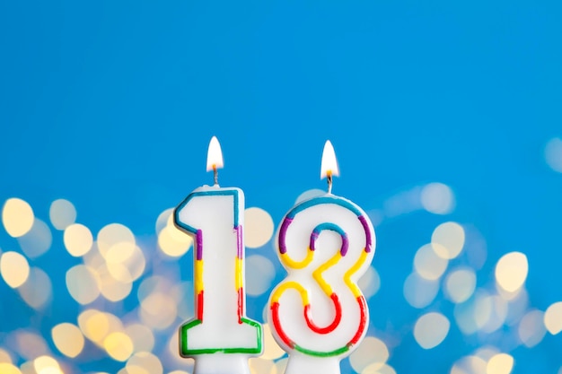 Photo bougie de célébration d'anniversaire du numéro 13 contre des lumières lumineuses et un fond bleu