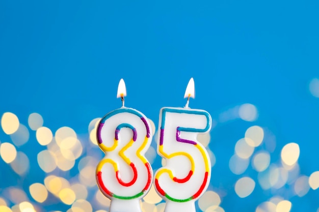 Bougie de célébration d'anniversaire du numéro 35 contre des lumières lumineuses et un fond bleu