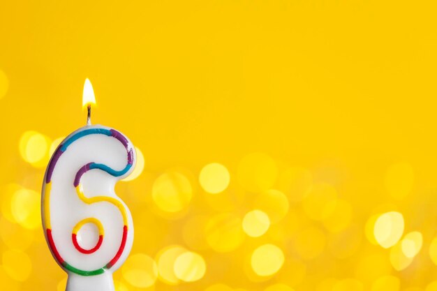 Bougie de célébration d'anniversaire du numéro 6 contre des lumières lumineuses et un fond jaune