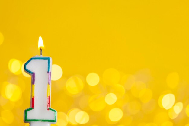 Photo bougie de célébration d'anniversaire numéro 1 contre une lumière vive et un fond jaune