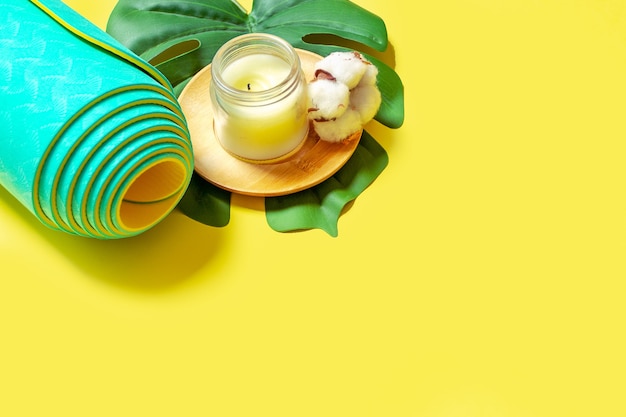 Bougie en cire avec du coton et tapis de yoga roulé à la menthe sur fond jaune