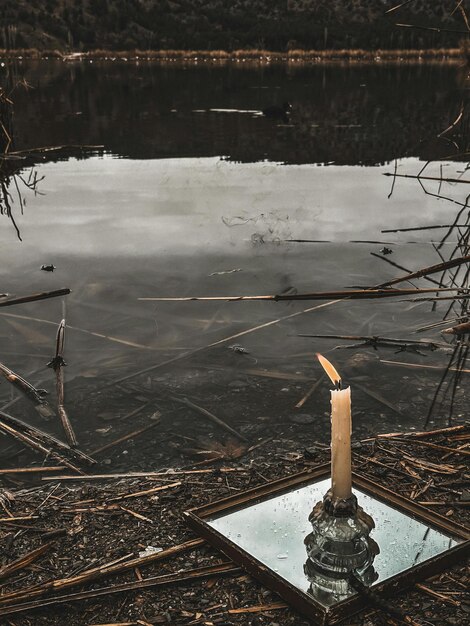 Photo une bougie est dans un cadre avec un reflet du ciel et des arbres dans l'eau