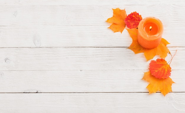 Bougie avec des feuilles d'automne sur un mur en bois blanc