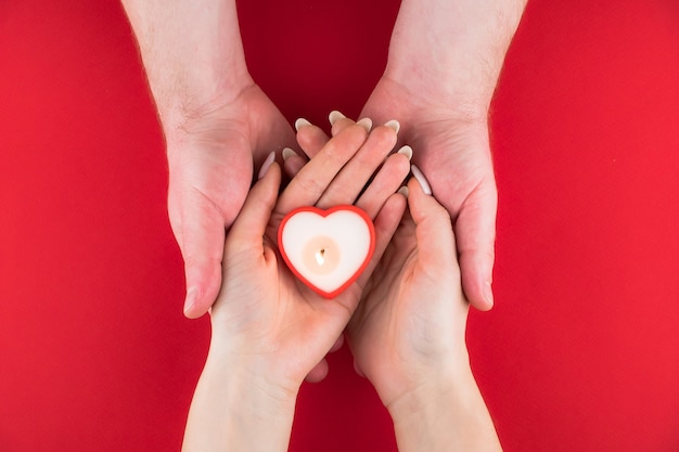 Bougie en forme de coeur dans les mains d'un couple sur une surface rouge pour la Saint Valentin