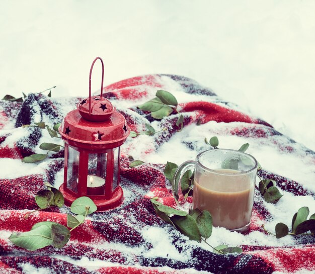 Bougie rouge festive dans une lanterne et une tasse de café sur un tapis avec de la neige