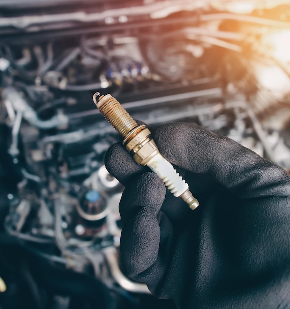 Photo les bougies d'allumage en iridium automobile sont détenues par la main d'un mécanicien automobile avec un arrière-plan flou dans le compartiment moteur et la lumière du soleil