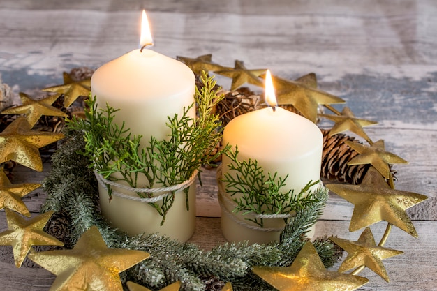 Bougies allumées avec une branche de sapin et des pommes de pin avec une couronne dorée autour