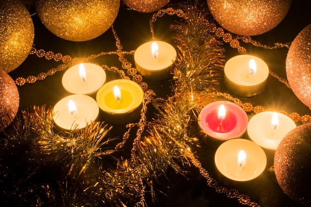 Bougies allumées entourées de boules brillantes et décor sur fond sombre