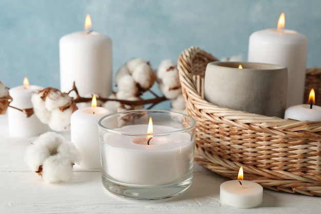 Bougies allumées, panier et coton sur bois blanc, gros plan