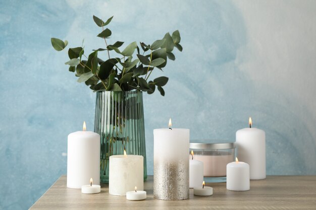 Bougies allumées et vase avec eucalyptus sur table en bois sur bleu