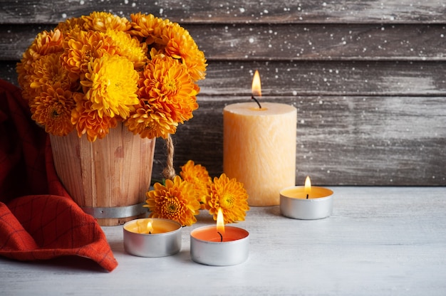 Bougies aromatiques allumées et fleurs orange sur table rustique.