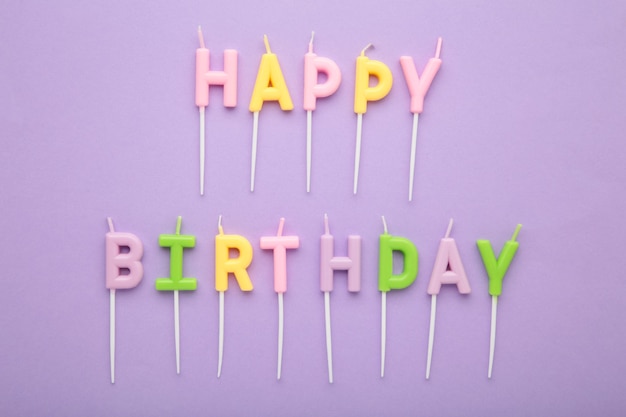 Bougies colorées en lettres disant joyeux anniversaire sur fond violet
