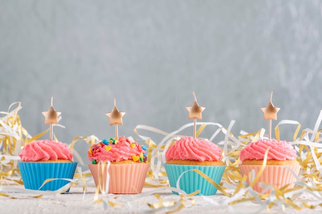 Bougies dorées en forme d'étoile sur les cupcakes Muffins avec glaçage à la crème au beurre rose sur fond de guirlandes festives Copier l'espace sur le mur gris